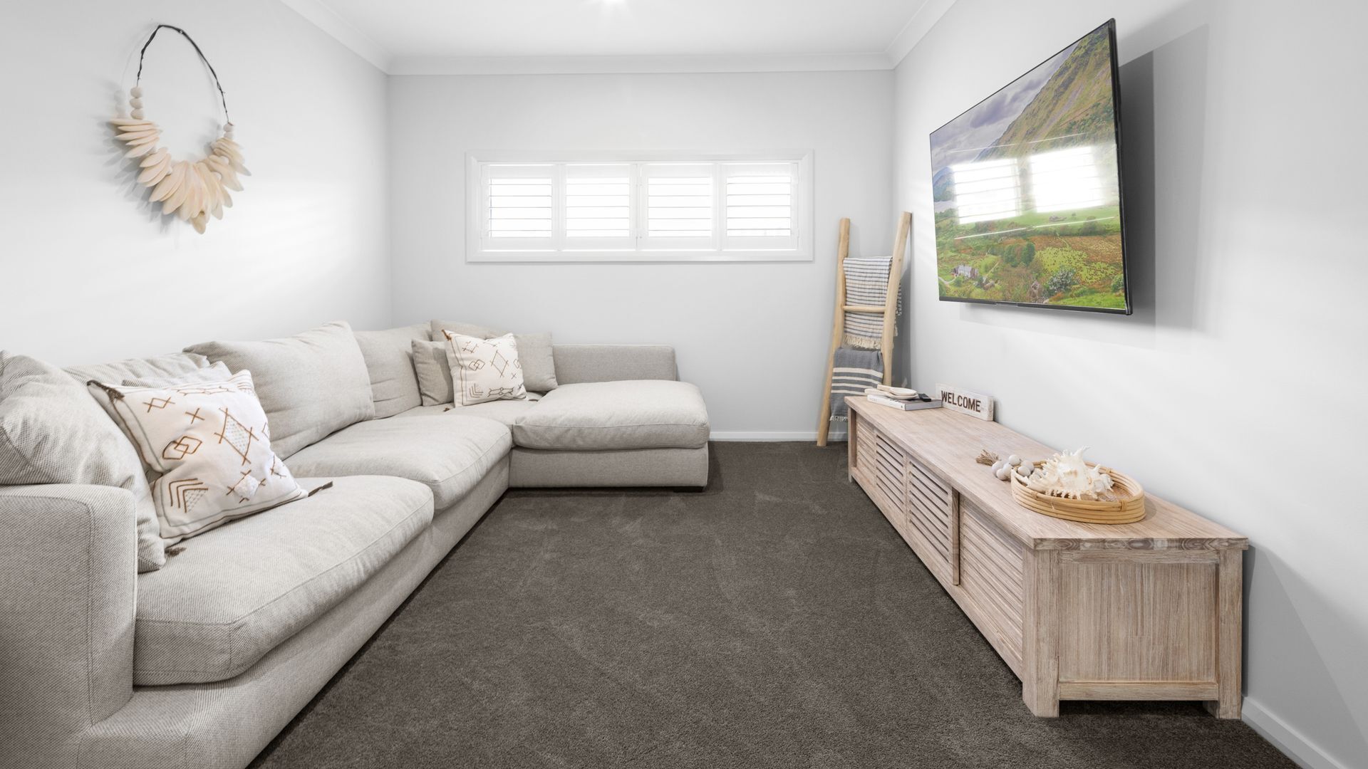 A modern living room with a sectional sofa, a wooden console table, a painting, and a window with blinds.