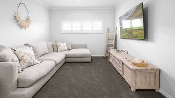 A modern living room with a sectional sofa, a wooden console table, a painting, and a window with blinds.