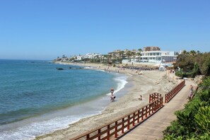 A beach with a wooden walkway, clear blue water, and buildings in the background.