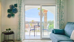 A balcony with a view of palm trees and a building, a blue sofa, a small table with a plant, and a decorative wall piece. - Modern 2 bed apartment Riviera close to the beach (Mijas Costa)