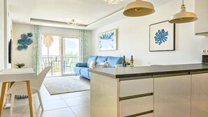 A modern kitchen with a central island, a dining area with a white table and wicker chairs, and a living area with a blue sofa. - Modern 2 bed apartment Riviera close to the beach (Mijas Costa)