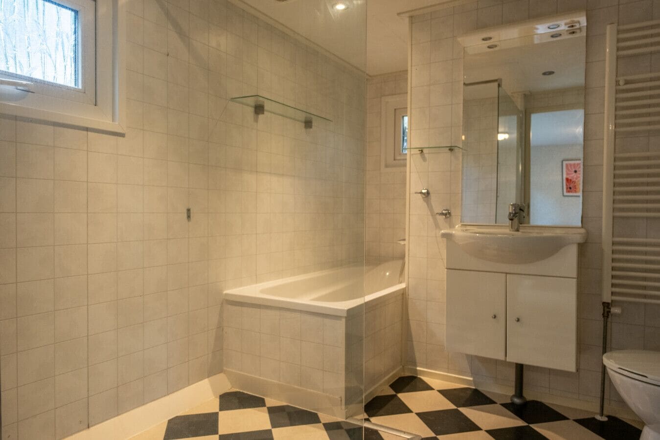 A bathroom with a checkered floor, a bathtub, a glass shower enclosure, and a sink with a mirror.