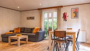 A modern living room with a grey sofa, wooden coffee table, and a dining area with a wooden table and chairs.