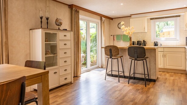 A kitchen with a wooden table, two bar stools, a cabinet with glass doors, and a window with curtains.
