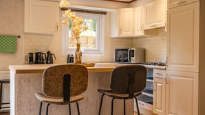 A kitchen with white cabinets, a central island with two bar stools, a microwave, and a gas stove.