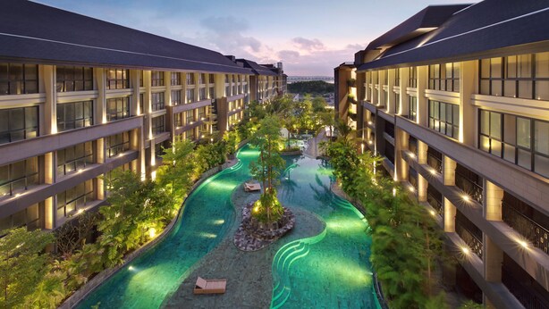 Un hotel moderno con piscina central, rodeado de exuberante vegetación y múltiples pisos de balcones.