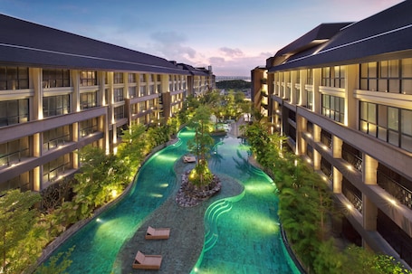 A modern hotel with a central swimming pool, surrounded by lush greenery and multiple floors of balconies.