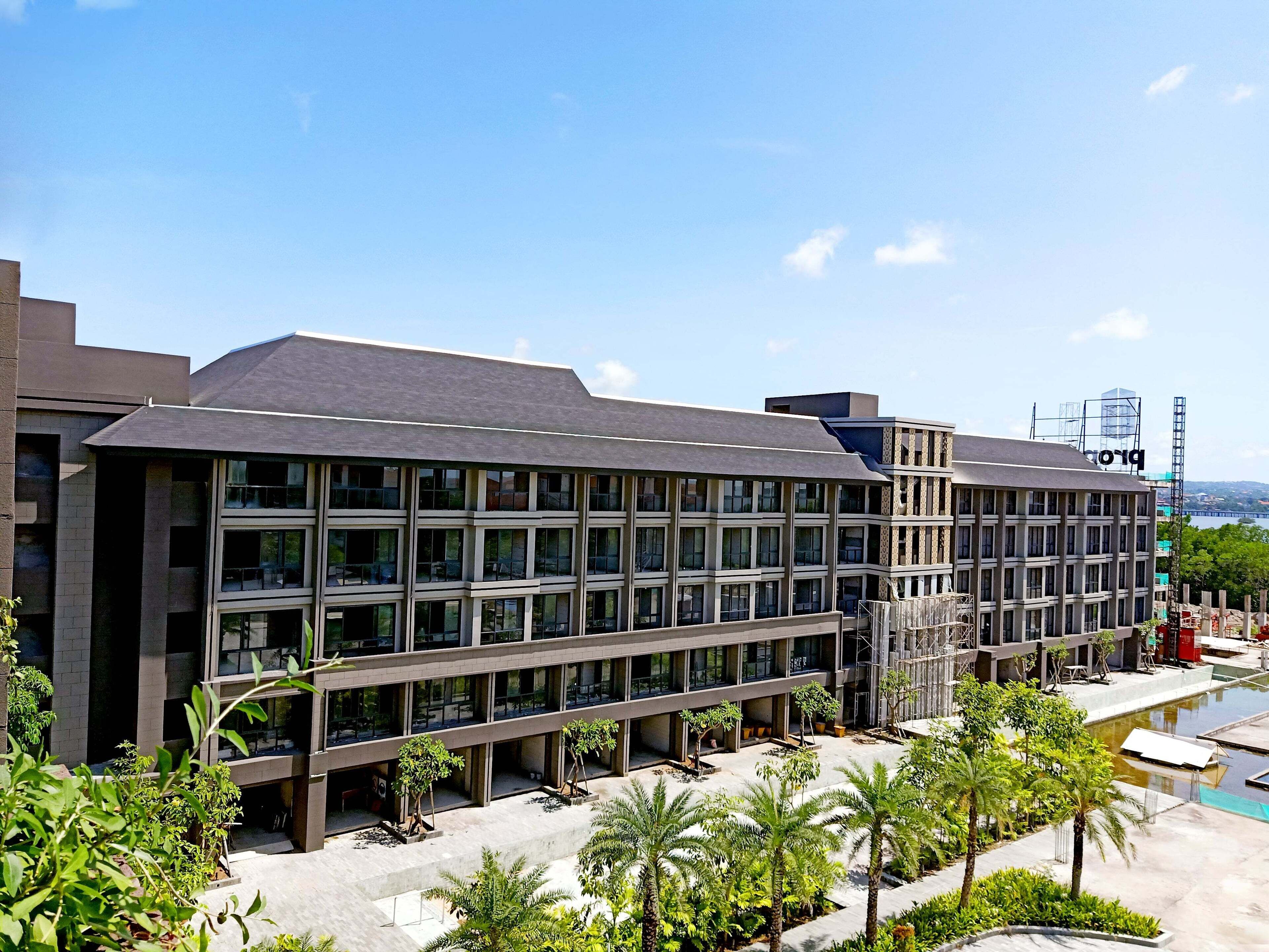 Un hôtel moderne doté d’un toit plat, de plusieurs étages et d’une cour intérieure agrémentée de palmiers et d’une piscine.