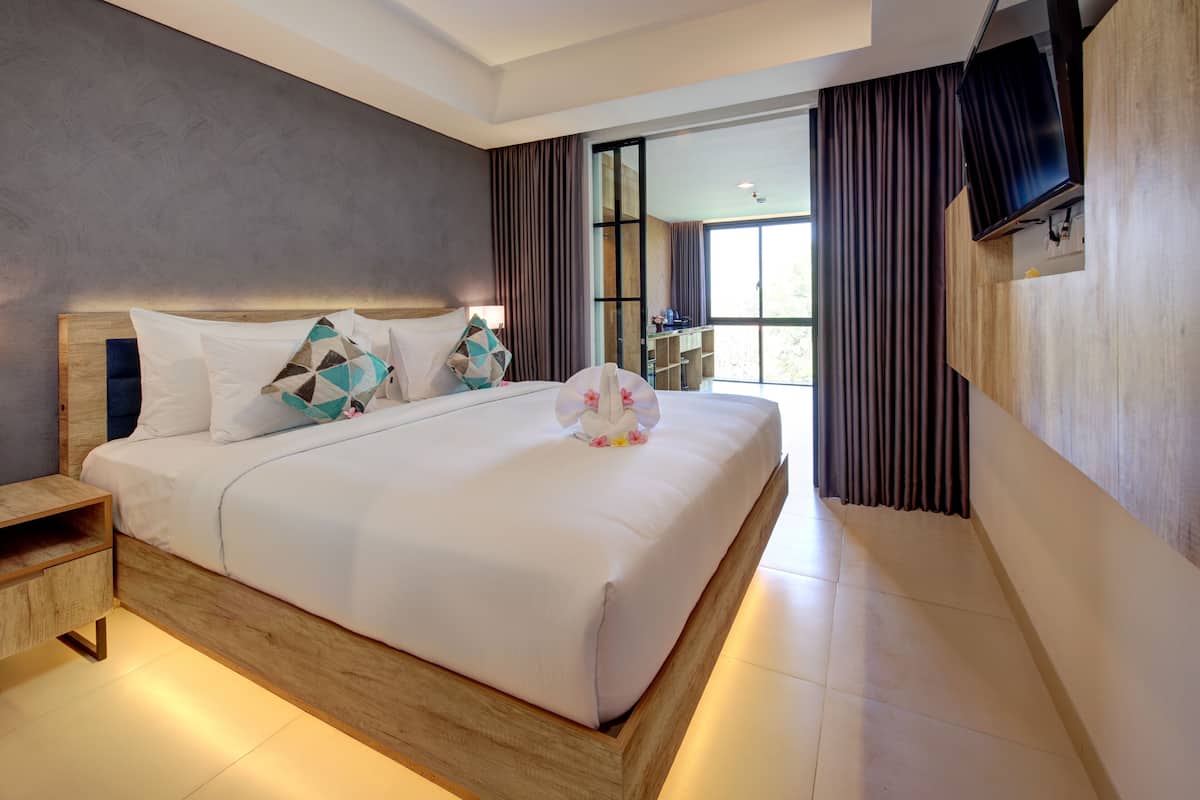 Een moderne hotelkamer met een groot bed, een houten hoofdeinde en een aan de muur bevestigde televisie.