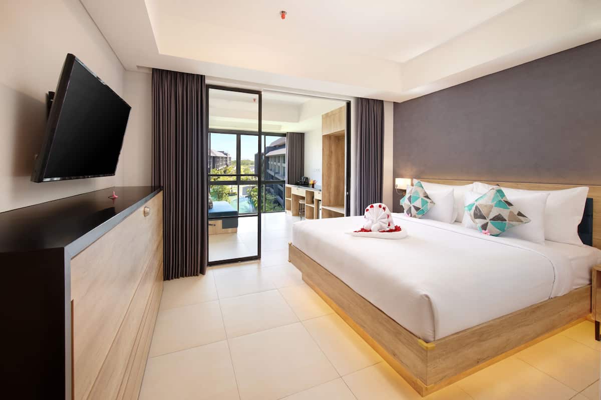 Een moderne hotelkamer met een groot bed, een flatscreen televisie aan de muur bevestigd, een glazen schuifdeur naar een balkon en een houten hoofdbord.
