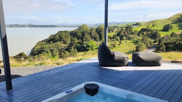 A hot tub on a wooden deck with a view of a lake and hills.