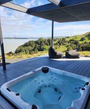 A hot tub on a wooden deck with a view of a lake and hills.