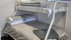 A bunk bed with a window above it, white walls, and a small window on the adjacent wall.