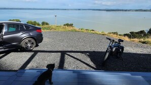A car parked on a gravel road with a view of a body of water and hills in the distance.