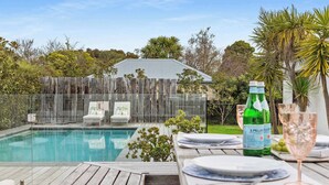 En have med swimmingpool, træterrasse, lukket opholdsområde med glas og et hegn.