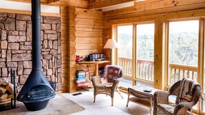 A cozy cabin interior with a stone fireplace, wicker furniture, and a balcony with a view of the forest. - Stunning Views & Starry Skies Deck & BBQ (Pine)