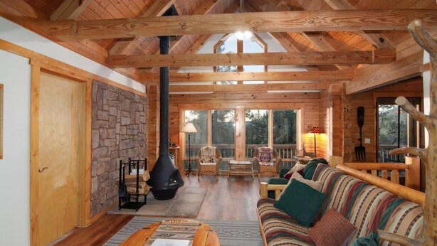 A log cabin interior with a stone wall, wooden ceiling beams, a large fireplace, a sofa, and a dining table. - Stunning Views & Starry Skies Deck & BBQ (Pine)