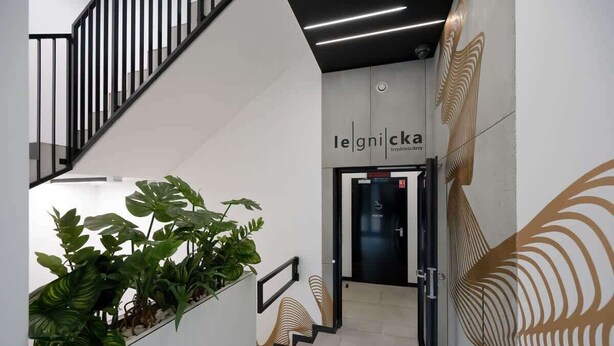 Een modern interieur met een trap, potplanten en een deur met de tekst 'legnicka'.