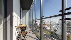 A balcony with a table and chairs, large windows offering a city view. - Elegant Apartment with Balcony | Parking and City View (Warszawa)
