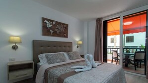 Ein Hotelzimmer mit einem großen Bett, zwei Nachttischlampen, einer Weltkarte als Wandbild und einem Balkon mit Sitzgelegenheiten.