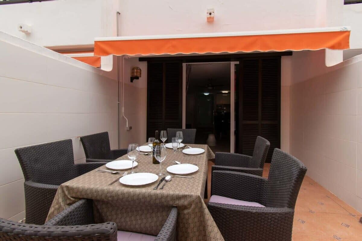 Un coin repas avec une table dressée pour six personnes, entourée de chaises en osier.