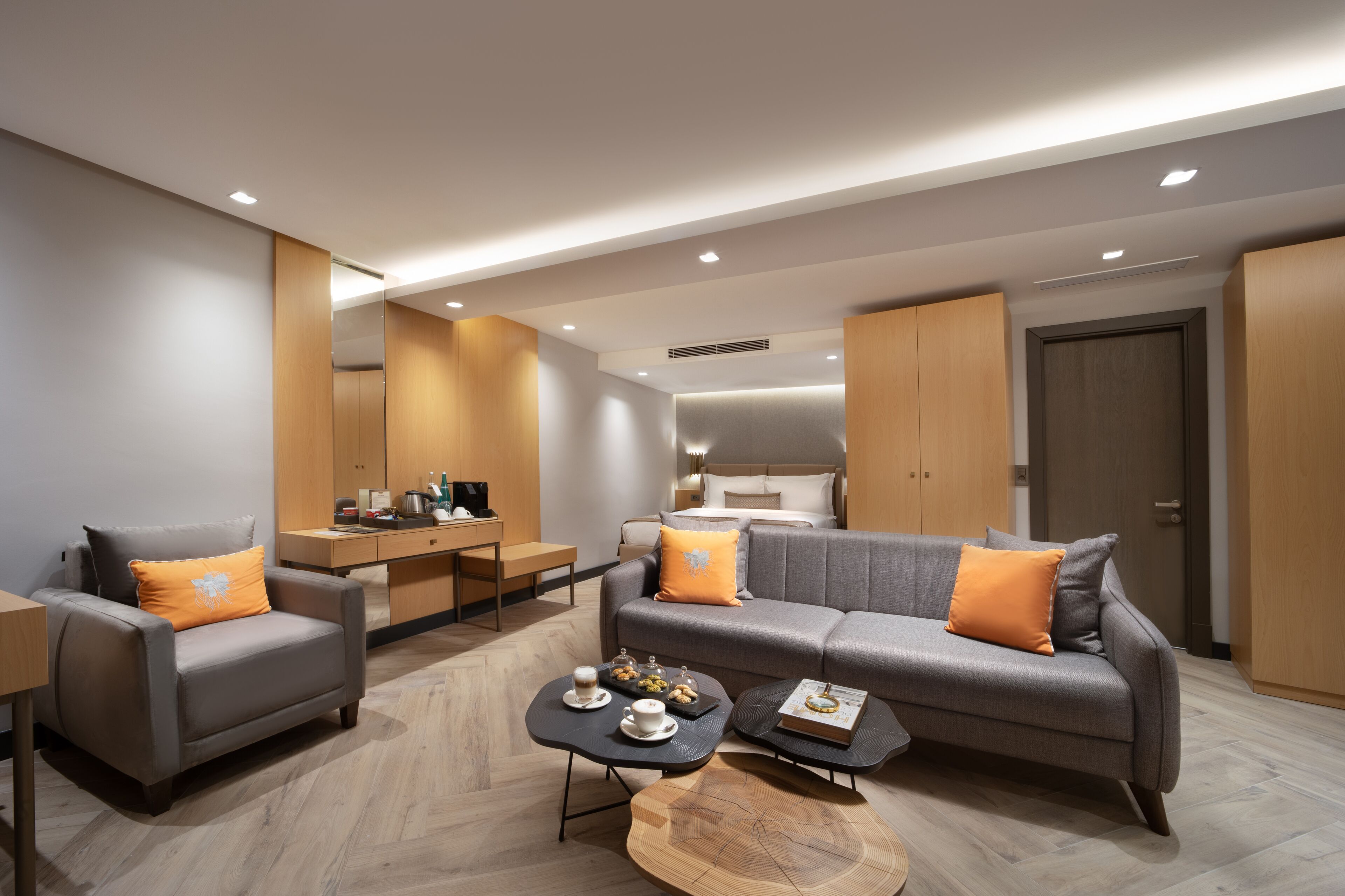 Una sala moderna con un sofá gris, un sillón gris y una mesa de centro de madera. Hay una pequeña zona de cocina con una mesa de comedor y sillas.