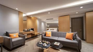 Una sala moderna con un sofá gris, un sillón gris y una mesa de centro de madera. Hay una pequeña zona de cocina con una mesa de comedor y sillas.