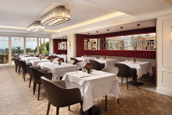 Ein Restaurant mit mehreren Tischen und Stühlen, großen Fenstern und Blick ins Freie.