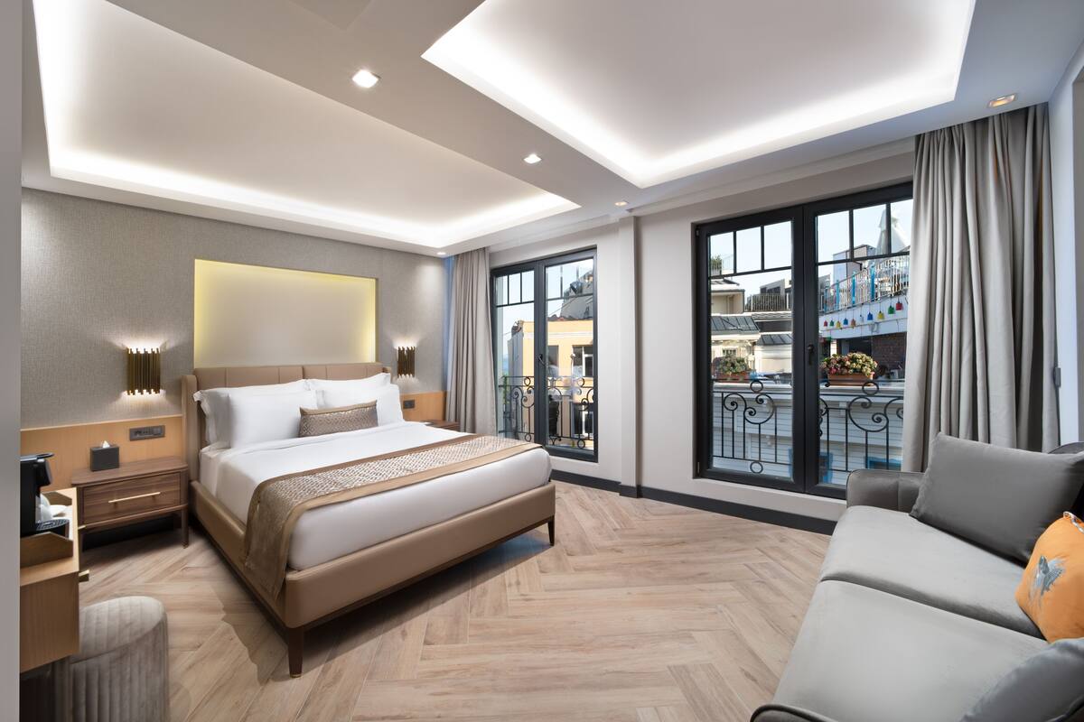 A modern hotel room with a large bed, a sofa, and a balcony with a view of the city.