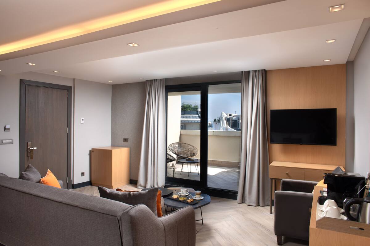A modern hotel room with a sofa, dining table, and a flat-screen TV.
