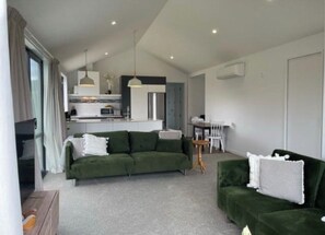 Relax in this stylish living area with a green sofa, coffee table, and dining table, featuring a modern kitchen with white cabinetry and stainless steel appliances.