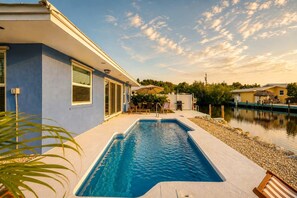 A swimming pool with a clear blue water feature, surrounded by a patio area with outdoor furniture and a view of a lake. - Dog-Friendly • Pool & Boat Dock • Sombrero Beach (Marathon)