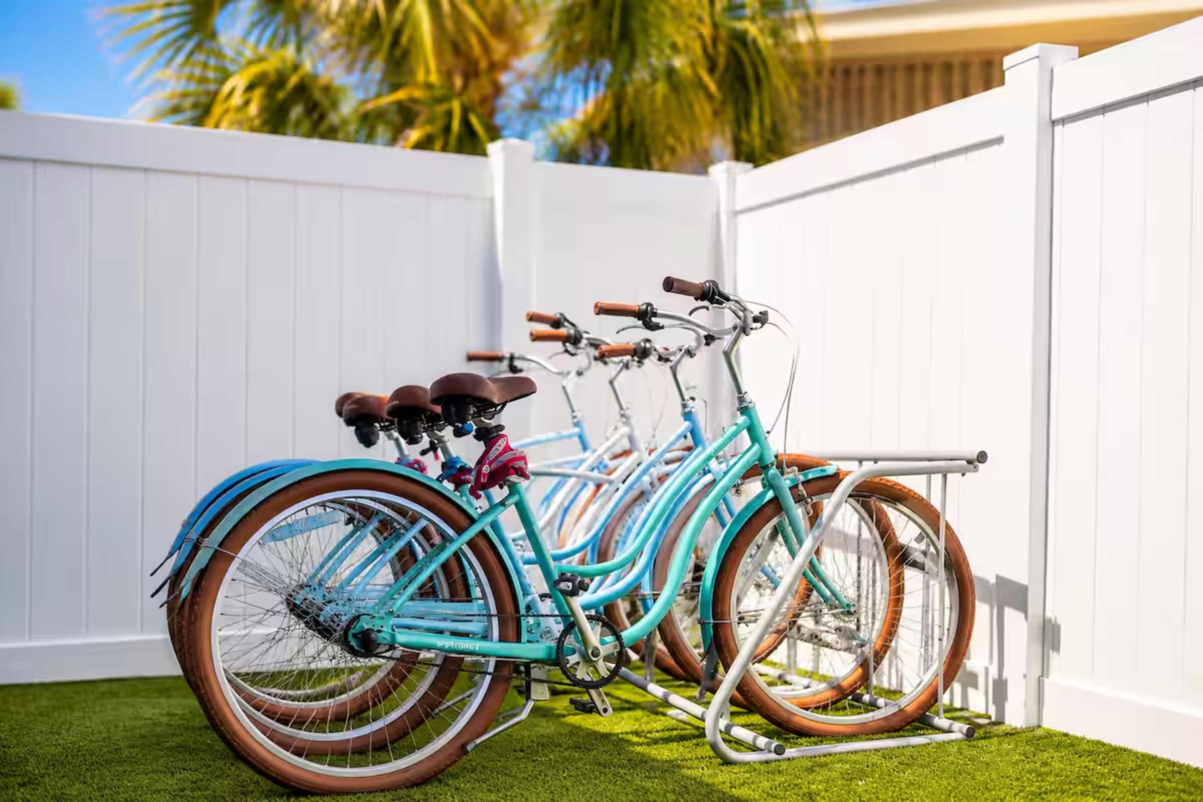 A row of bicycles parked against a white fence with a grassy area in front.