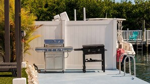 A waterfront outdoor area with a grill and a table, a dock with a boat, and a white fence. - Dog-Friendly • Pool & Boat Dock • Sombrero Beach (Marathon)
