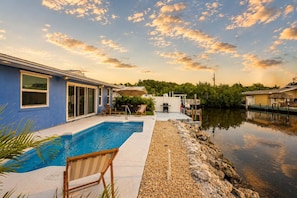 A swimming pool with lounge chairs, a deck, and a view of a body of water and greenery. - Dog-Friendly • Pool & Boat Dock • Sombrero Beach (Marathon)