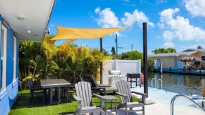 A patio with a table and chairs, a grill, and a poolside area with a ladder. - Dog-Friendly • Pool & Boat Dock • Sombrero Beach (Marathon)