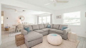 A modern living room with a sectional sofa, a round ottoman, a ceiling fan, and a dining area with a table and chairs. - Dog-Friendly • Pool & Boat Dock • Sombrero Beach (Marathon)