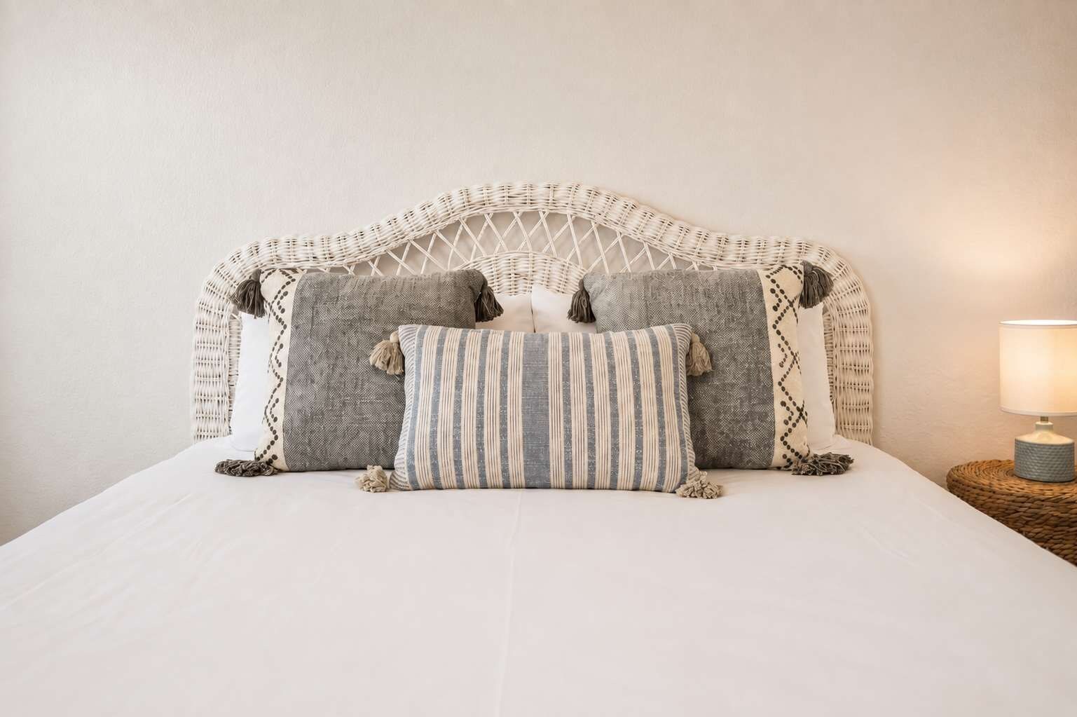 A bed with a woven headboard, multiple pillows, and a bedside lamp.