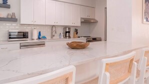 A modern kitchen with white cabinetry, a marble countertop, and a central island with a wooden bowl. - Dog-Friendly • Pool & Boat Dock • Sombrero Beach (Marathon)