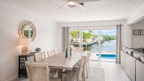A dining area with a table and chairs, a ceiling fan, and a view of a water body through large glass doors. - Dog-Friendly • Pool & Boat Dock • Sombrero Beach (Marathon)