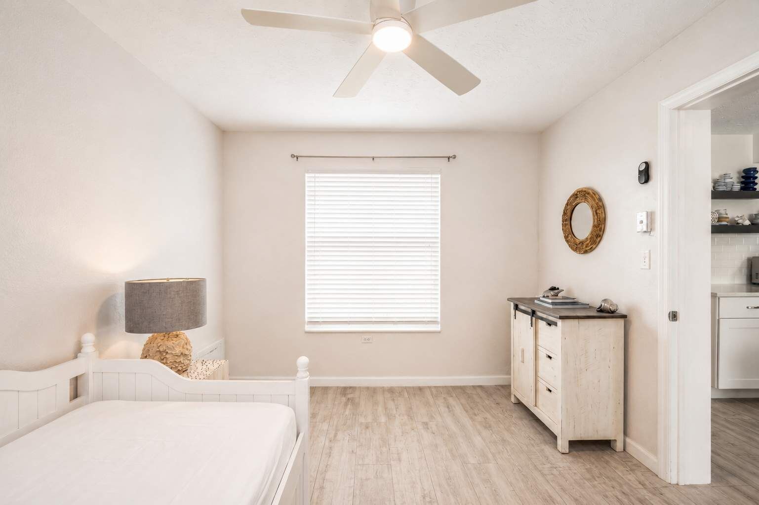 A bedroom with a bed, bedside lamp, dresser, and a ceiling fan.