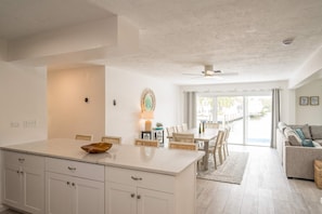 A modern kitchen with white cabinetry, a central island, and a dining area with a view of the outdoors. - Dog-Friendly • Pool & Boat Dock • Sombrero Beach (Marathon)