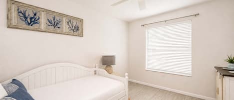 Een slaapkamer met een bed, een plafondventilator, een raam met jaloezieën en een kunstwerk aan de muur.