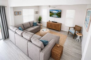 A modern living room with a sectional sofa, a flat-screen TV, a wooden cabinet, and a wicker ottoman. - Dog-Friendly • Pool & Boat Dock • Sombrero Beach (Marathon)