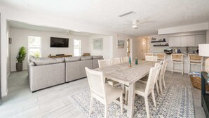 A modern living room with a sofa, TV, and dining area with chairs and a table. - Dog-Friendly • Pool & Boat Dock • Sombrero Beach (Marathon)