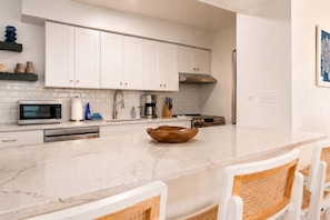 A modern kitchen with white cabinetry, a marble countertop, and a central island with a wooden bowl. - Dog-Friendly • Pool & Boat Dock • Sombrero Beach (Marathon)