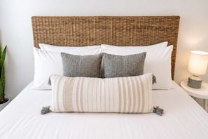 A bed with a woven headboard, two pillows, a striped throw pillow, and a bedside lamp. - Dog-Friendly • Pool & Boat Dock • Sombrero Beach (Marathon)