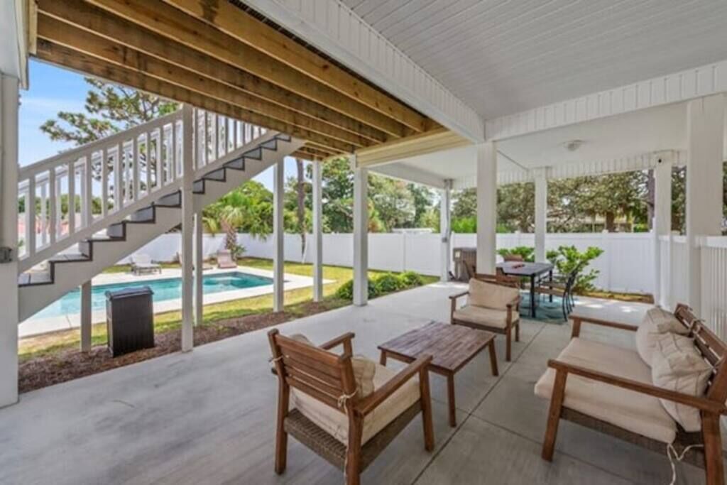 Eine überdachte Terrasse mit Holzmöbeln, einer Treppe und Blick auf einen Swimmingpool.