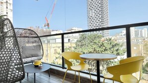 A balcony with a wicker chair, a small table with a lamp, and two yellow chairs. - Jerusalem 9 - By Beach Apartments TLV (Bat Yam)
