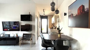 A modern living room with a flat-screen TV, a dining area with a table and chairs, and a kitchen in the background. - Jerusalem 9 - By Beach Apartments TLV (Bat Yam)
